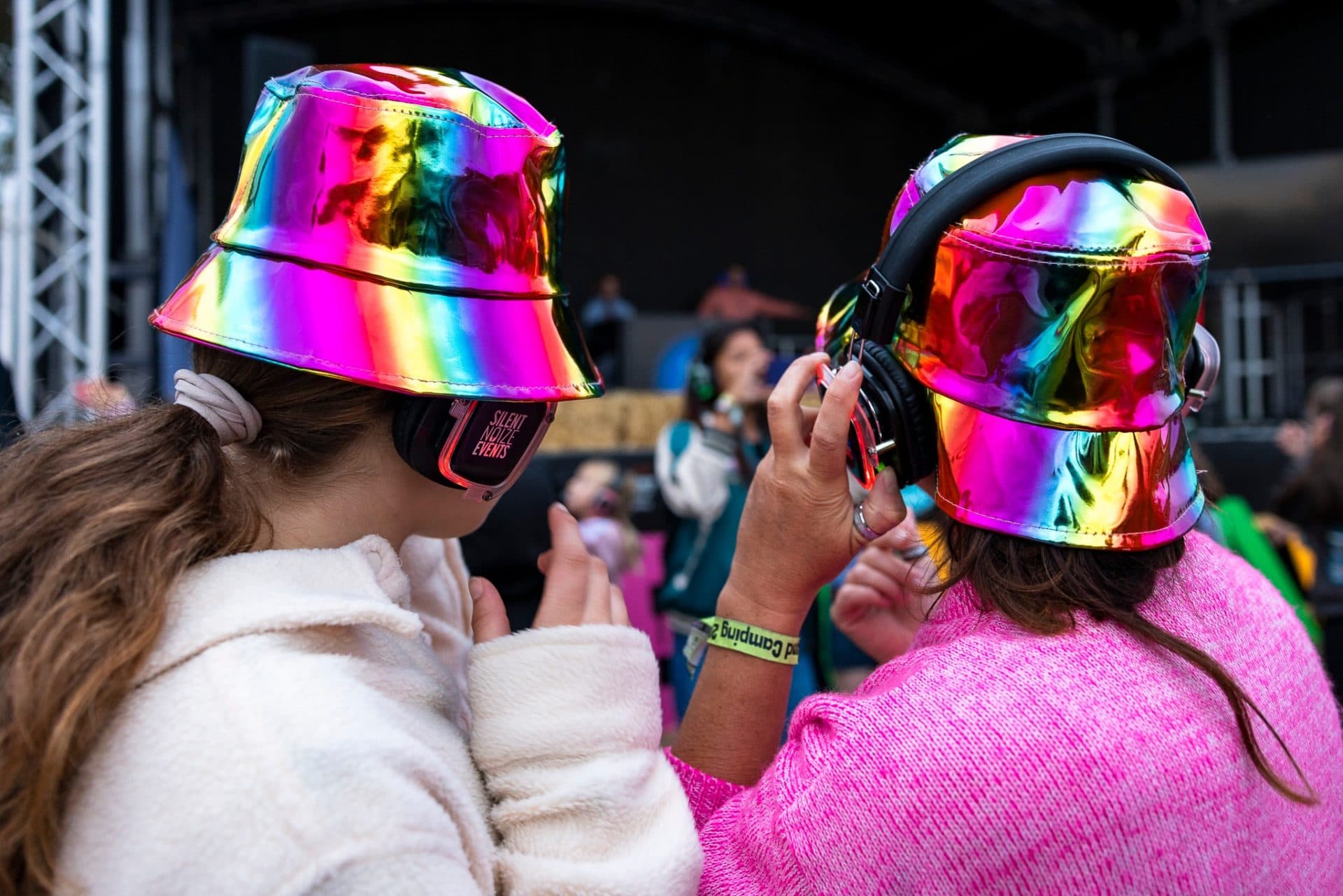 Two ladies in rainbow bucket hats and headphones